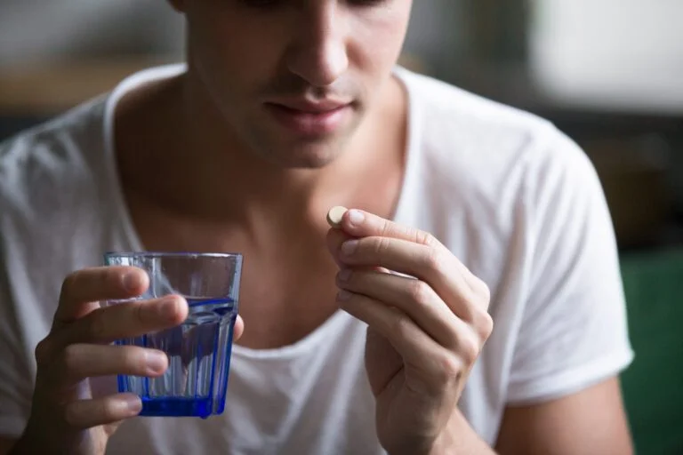 Hombre con una pastilla en la mano y un vaso de agua